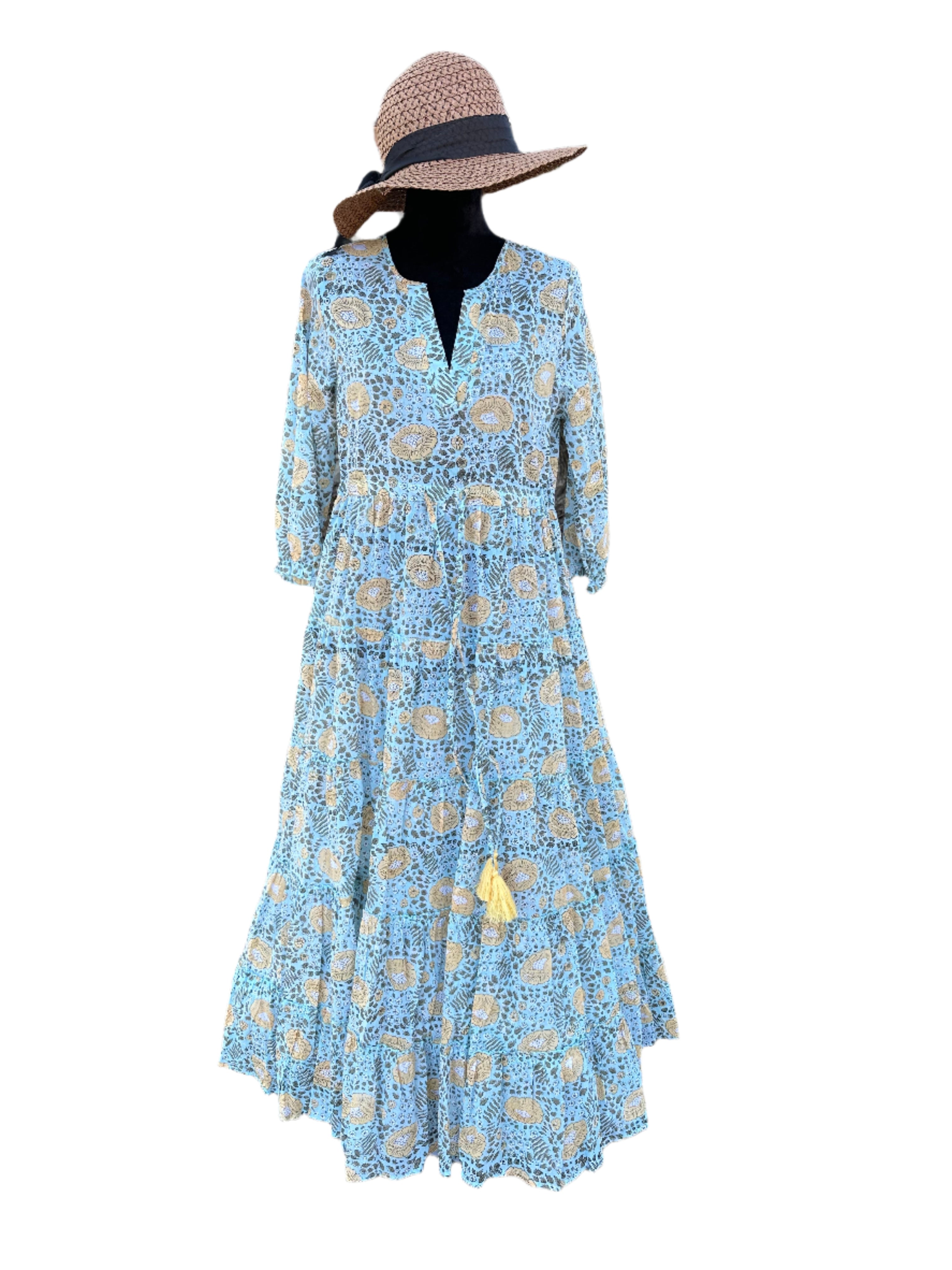 The dress in the image has a light blue base color with beige, white, and black floral patterns. There are also small yellow tassel accents. The overall color palette is soft, earthy, and vintage-inspired, giving it a timeless, bohemian look