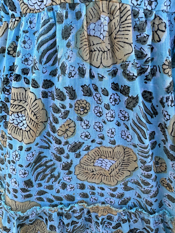 The fabric in the image has a light blue -Green base color with floral and botanical patterns in beige, black, and white. The design  has a hand-block printed traditional textile look, with earthy tones complementing the blue background.