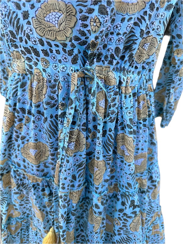 The fabric in the image has a light blue -Green base color with floral and botanical patterns in beige, black, and white. The design  has a hand-block printed traditional textile look, with earthy tones complementing the blue background.